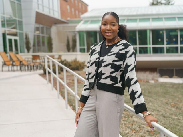 Olivia "Kaami" Effa stands outside of the student center wearing a black and white patterned cardigan and tan slacks.