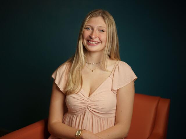 Headshot of Madge Myers on an orange couch while wearing a pink blouse.