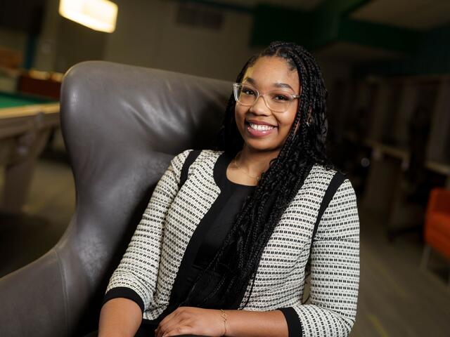 Nakayla Lawson sits in an armchair, wearing a black shirt and a black and white striped blazer.