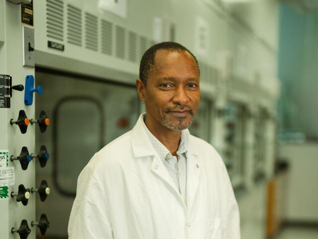 Katana Ngala stands in a college lab wearing a white lab coat.