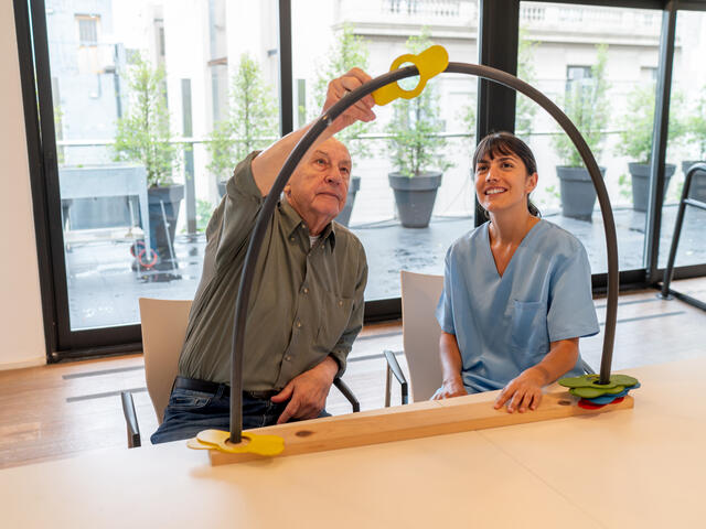 occupational therapist looks on while a patient manipulates an object around a dome shaped bar. 
