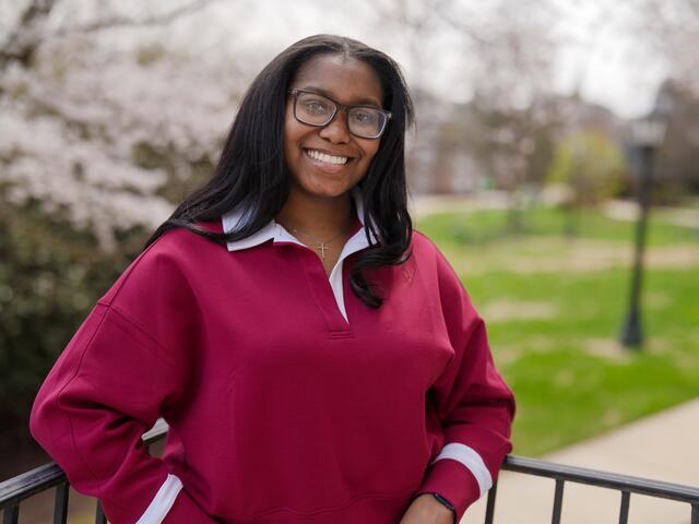 A female student in glasses smiles in front of flowering trees on the McDaniel campus.