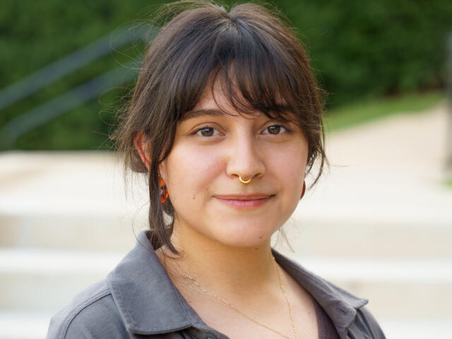 A young woman with dark hair smiles in a gray shirt.