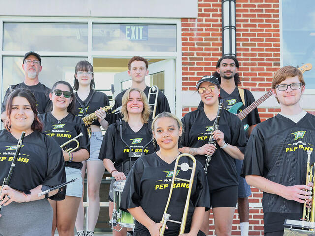 Students wearing Black t-shirts that say McDaniel College Pep Band pose with their instruments
