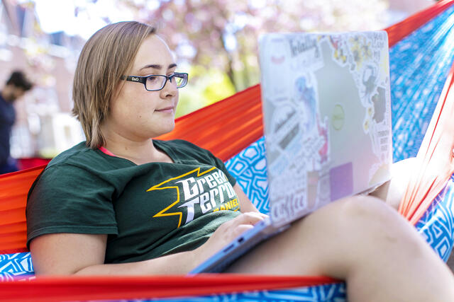 Student on computer in hammock on campus.