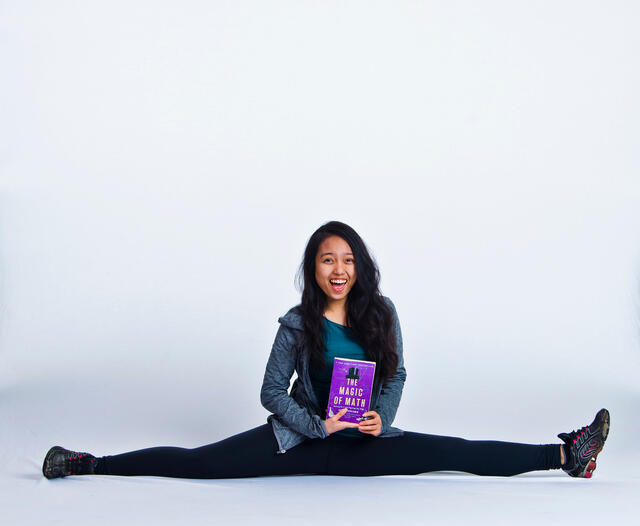 Angel Tuong holding a book while doing a split.