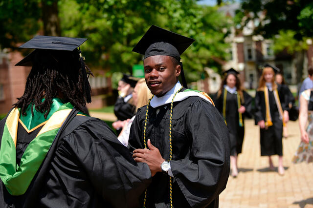 Graduates in cap and gown walking across campus.
