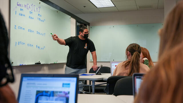 Student teaches other students at a whiteboard.