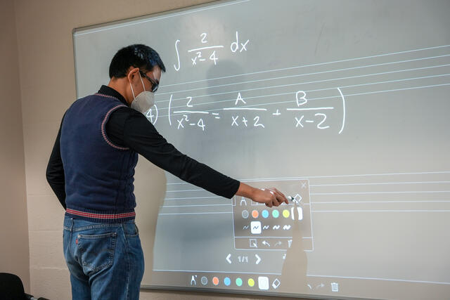 A student writes equations on a whiteboard.