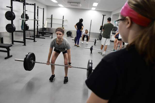 Student doing barbell deadlifts in an exercise classroom.