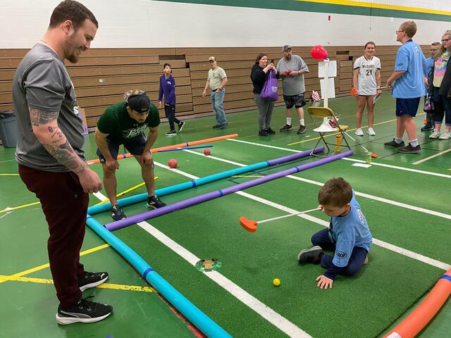 Two students help a child play indoor hockey at Tournament of Champions.