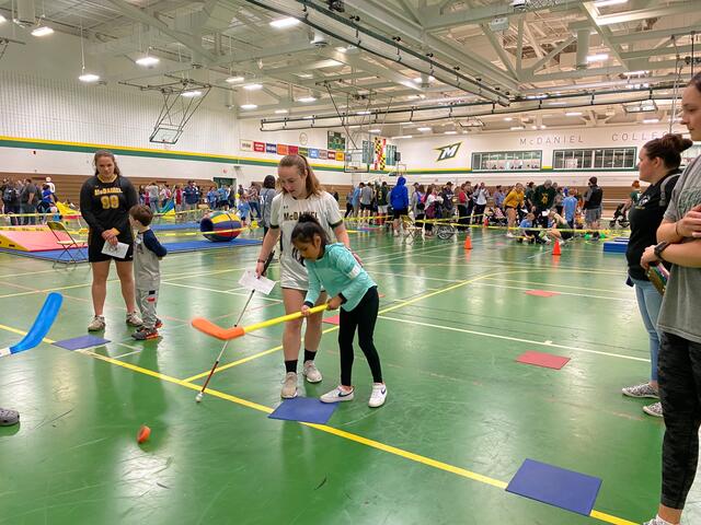 Student helps a child play hockey at Tournament of Champions. 