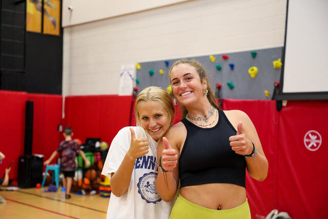 Two students pose with thumbs up.