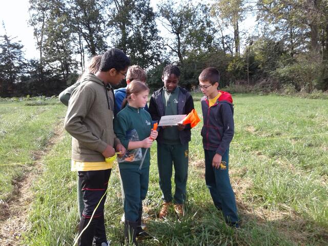 A group of students stand in a field, looking down at a map.