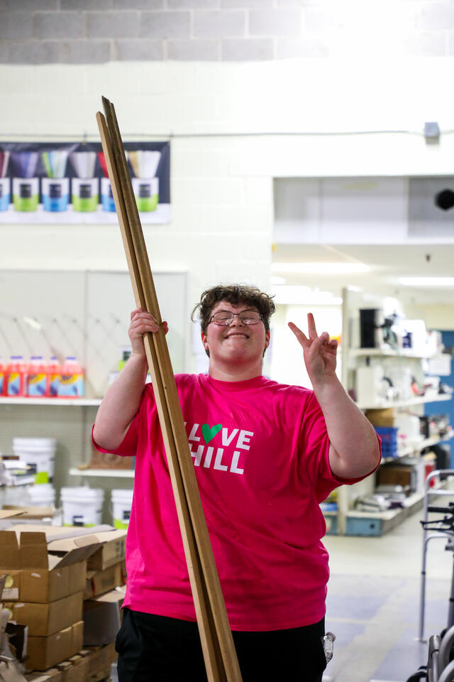 A student gives the peace sign while carrying a wooden beam at Habitat for Humanity ReStore.