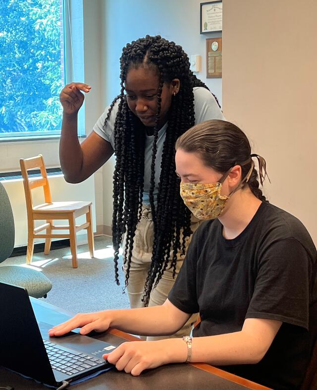 One student practices sign language next to another at a computer screen.