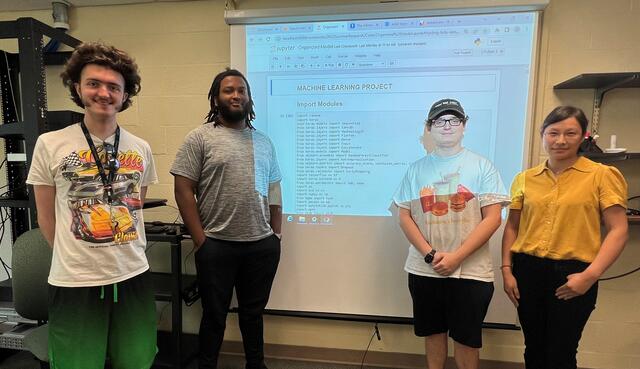 Three students pose with professors Zhang in front of a screen with computer code.