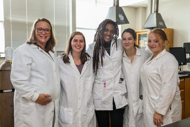 Professor Stephanie Homan poses with three students in the Chemistry lab.