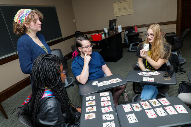 Peer mentor Sarah England stands by a group of students play a card game in a classroom.