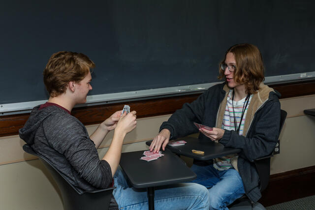Two students play a game of cards together in a classroom.