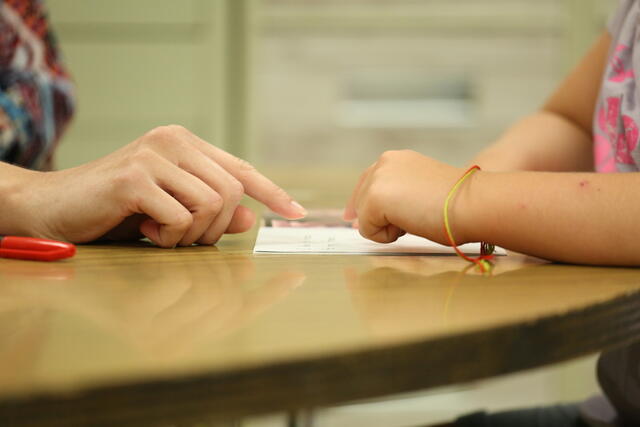 Close-up image of two hands pointing at a page, one set from a child and one of an adult.