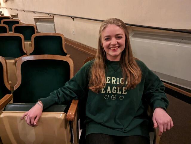 A student in a green sweatshirt sitting in theater seating 