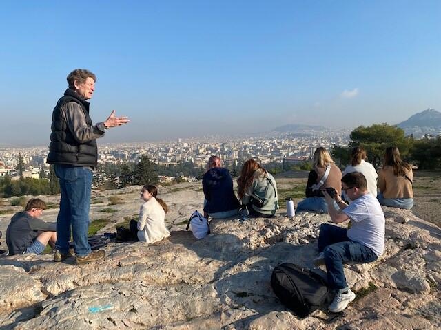 Students sitting on rocks overlooking a city in Greece