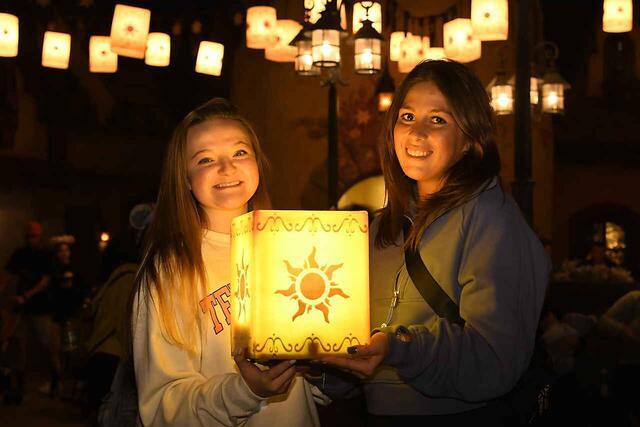 Two girls stand with a lantern in a dark room