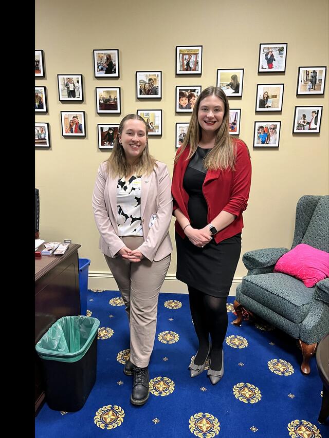 Two students in business attire pose in an office. 