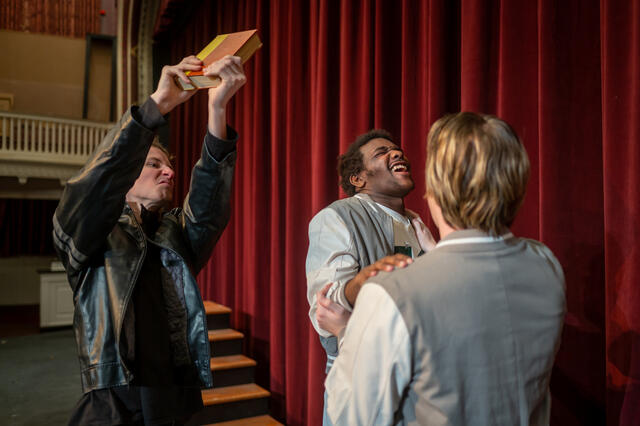 Three students staging a fight with a book 