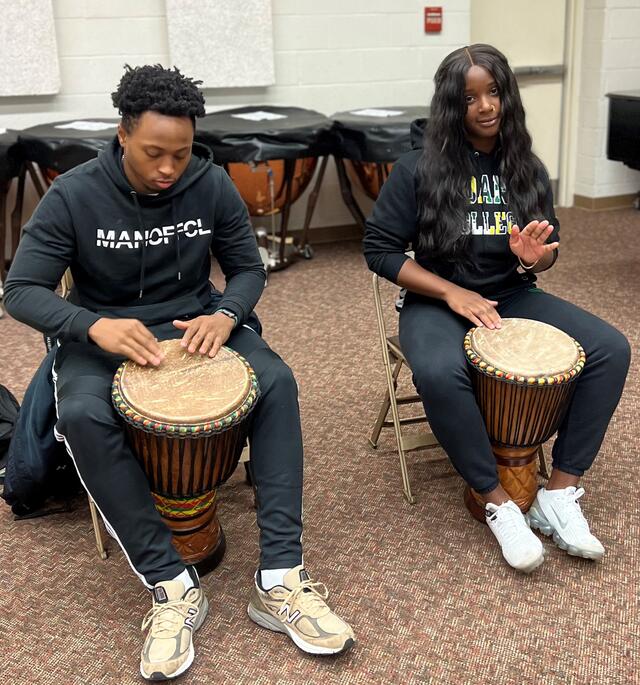 Two students playing djembe drums in the classroom.