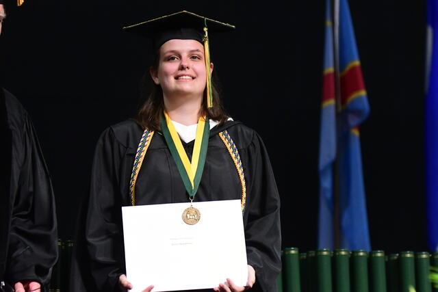 Photo of alum Kaitlyn Bowser in her graduation regalia holding a certificate for the Argonaut Award.