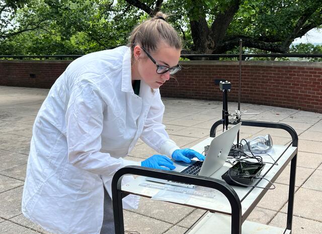 Student Angalyn Strouse looks at her laptop outside, where it is connected to a UV sensor.