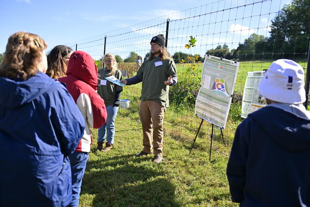 Students speak to a tour group at the McDaniel Environmental Center, standing in front of a sign about the forest garden.