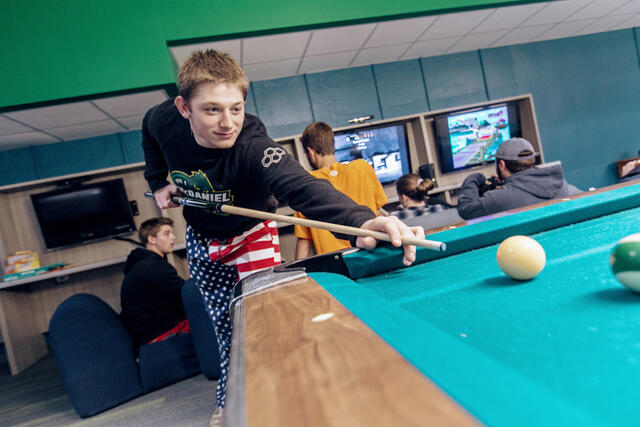 Student leaning over a pool table about to strike a ball.