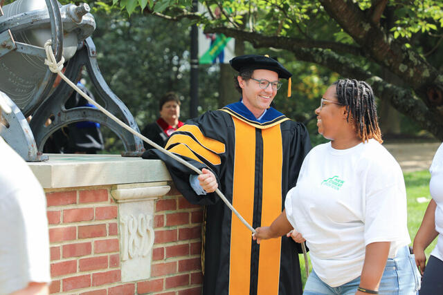 A student rings the bell with the provost standing beside it.