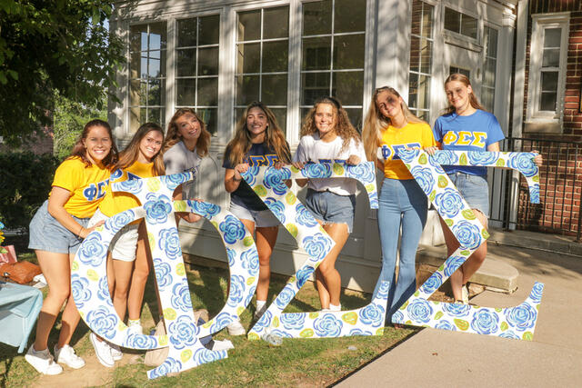 A group of sorority sisters stand holding large cutouts of their Greek organization name.
