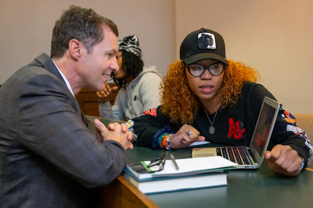 A Black, female student speaks to a white man while they look at a laptop screen.