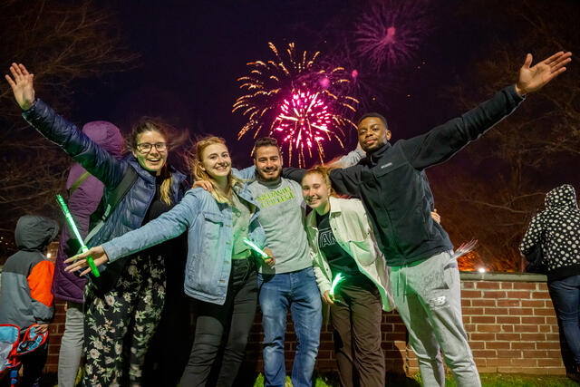 A group of McDaniel alumni stand in front of fireworks at night.