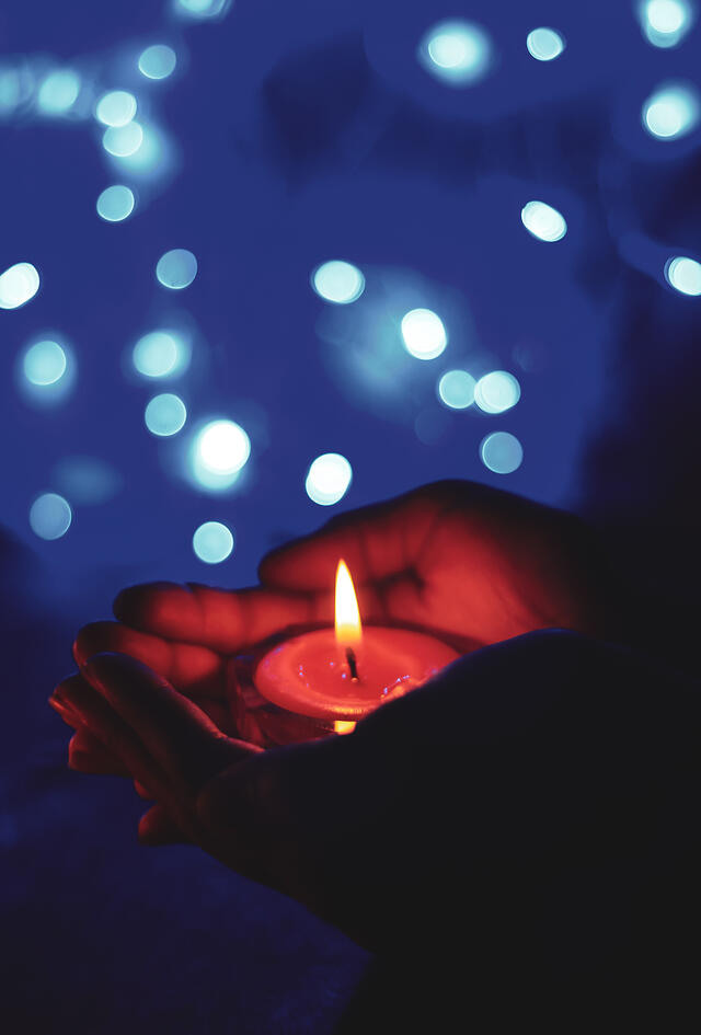 hands holding a tea light candle in the dark