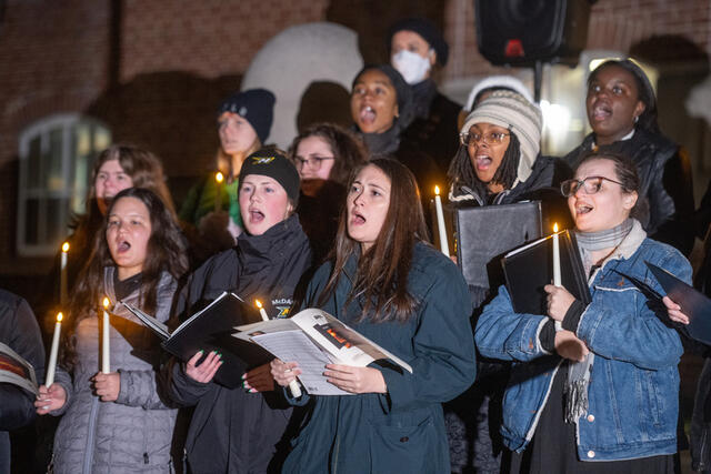 Students holding sheet music sing outdoors.