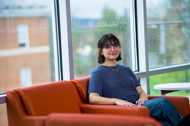 A student sits in an orange chair in front of a window.