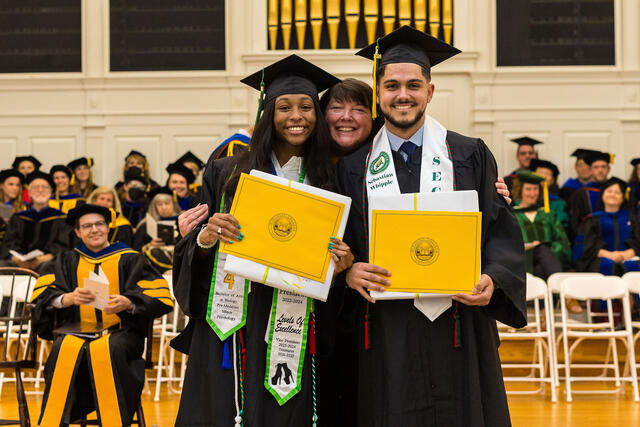 students in graduation regalia pose with awards