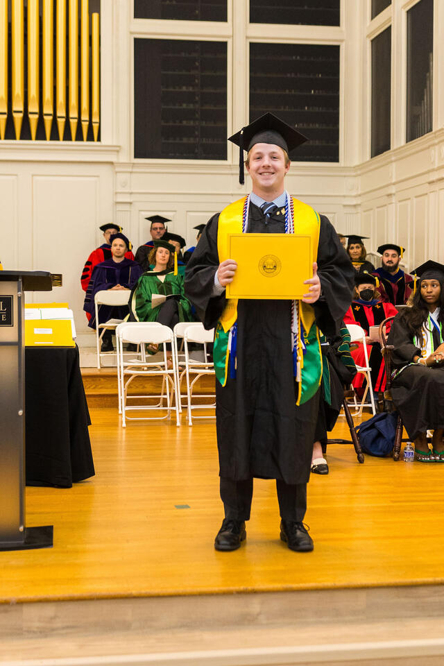 Student in graduation regalia holds up award