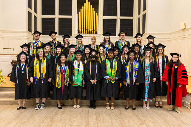 Students in regalia walk through the historical arch, led by the provost in regalia