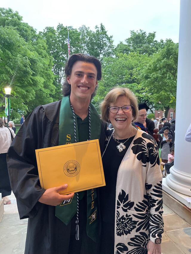 student in graduation regalia holds up award and poses with adult female