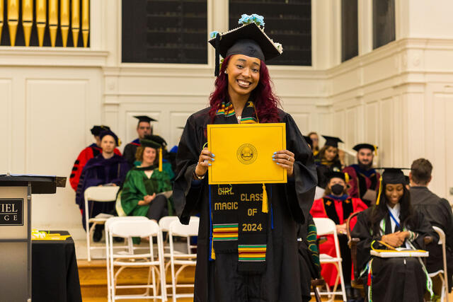 Student in graduation regalia holds up award