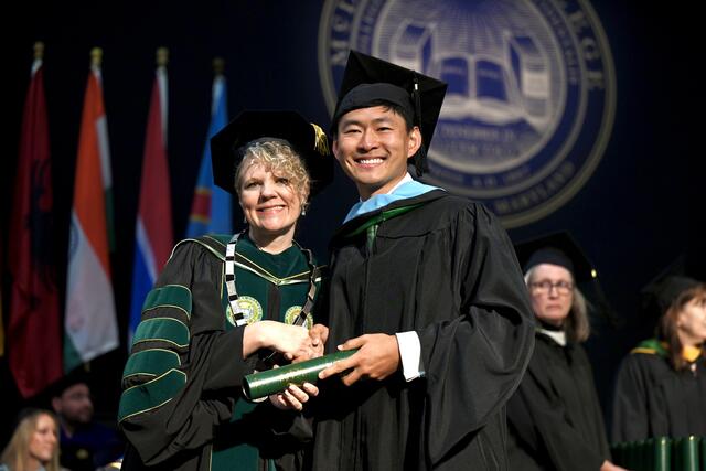 student poses for photo after receiving diploma