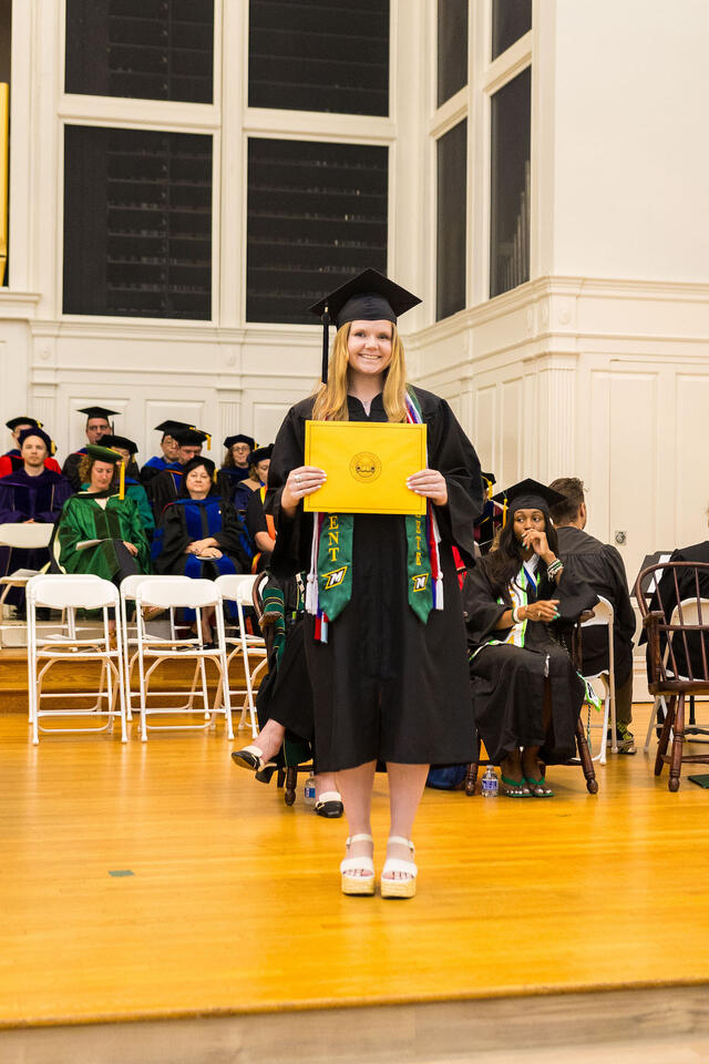 Student in graduation regalia poses with award