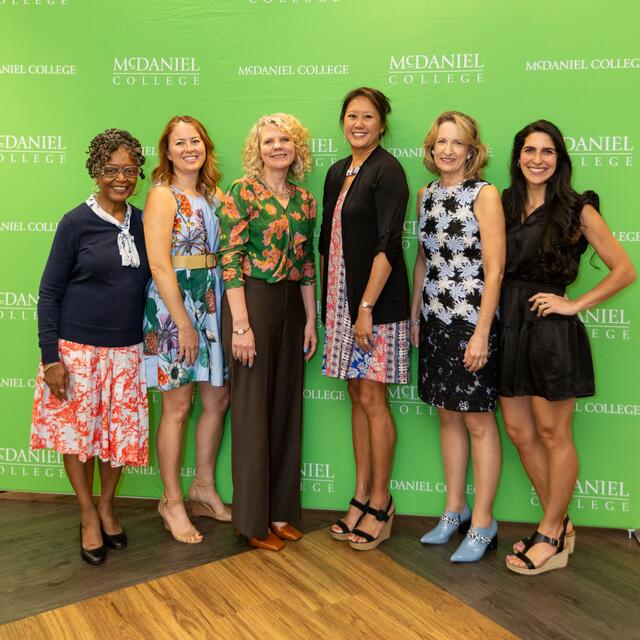Six women stand together smiling.